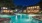 a pool with a fountain in front of a house at night
