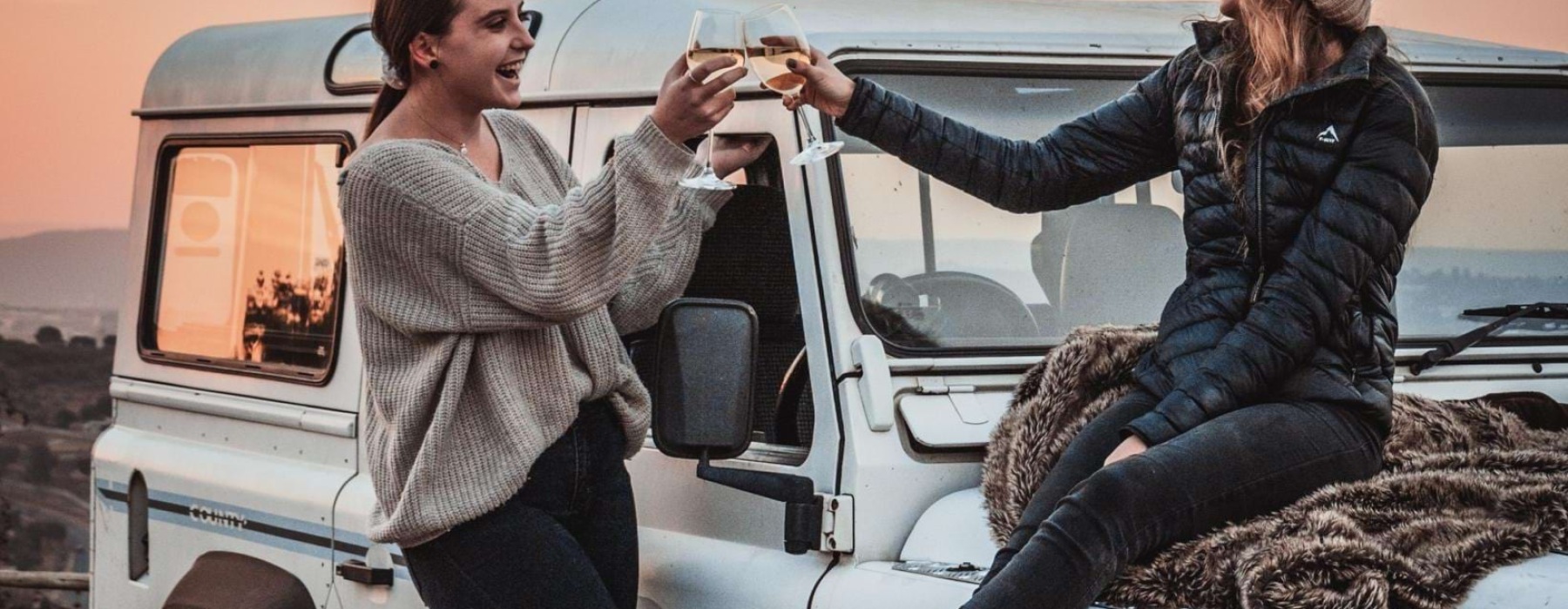 a person sitting on a car with another woman standing on the hood