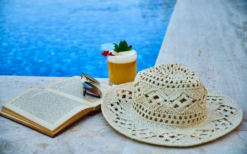 a hat and a book on a table by a pool