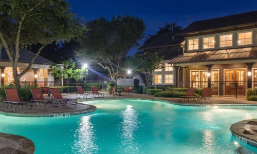 a pool with a fountain in front of a house at night