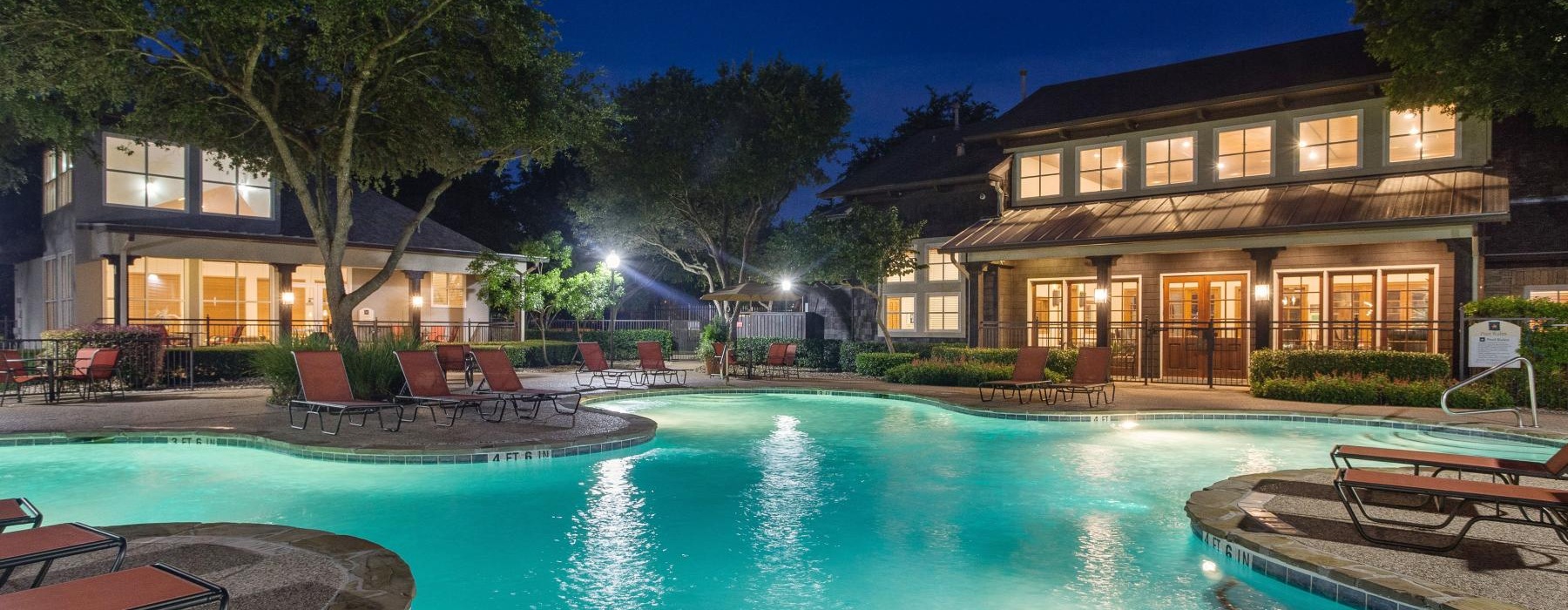 a pool with a fountain in front of a house at night